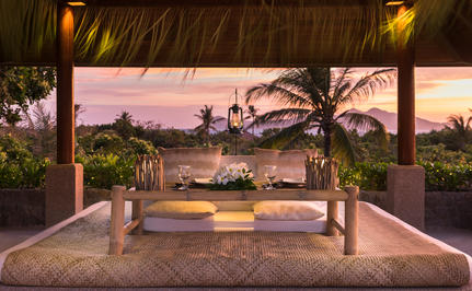 Covered sala at Amanpulo with dining table overlooking sunset views across the islands.