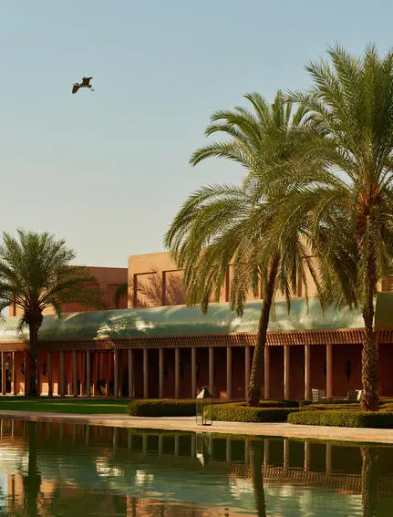 Palmiers bordant un canal à Amanjena, resort au Maroc, avec bâtiment en terre cuite en arrière-plan.