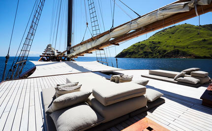 Amandira's sundeck with teak loungers and sailing rigging overlooking calm waters.