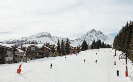 Skiers and snowboarders on snow-covered slopes at Aman Le Mélézin, with snow-capped mountains in the distance.