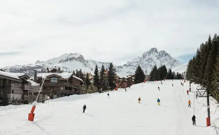 Skiers and snowboarders on snow-covered slopes at Aman Le Mélézin, with snow-capped mountains in the distance.