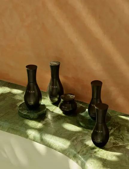 Quatre bougies parfumées noires Aman Skincare alignées sur une surface blanche à Amanjena, la station balnéaire de Marrakech.