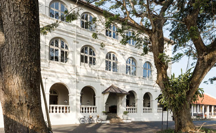 Amangalla's whitewashed colonial façade with arched windows and balustrade, framed by mature trees.