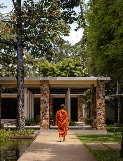 Buddhist monk in saffron robes walking through a stone pavilion at Amansara, Cambodia.