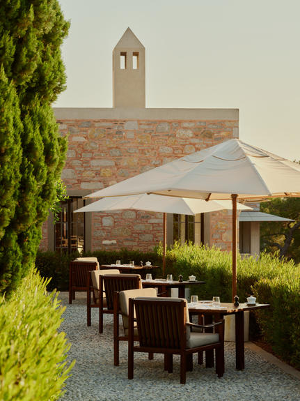 Poolside dining terrace at Amanruya with stone architecture, shaded seating and verdant landscaping.