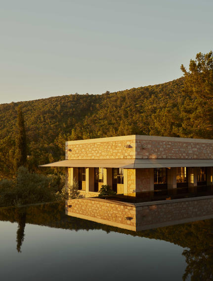 Amanruya's main pool and Ottoman lounge overlooking calm water at golden hour, surrounded by forested hillside.