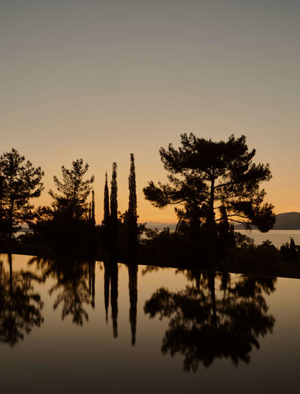 Silhouetted cypress and pine trees reflected in still water at Amanruya at sunset.