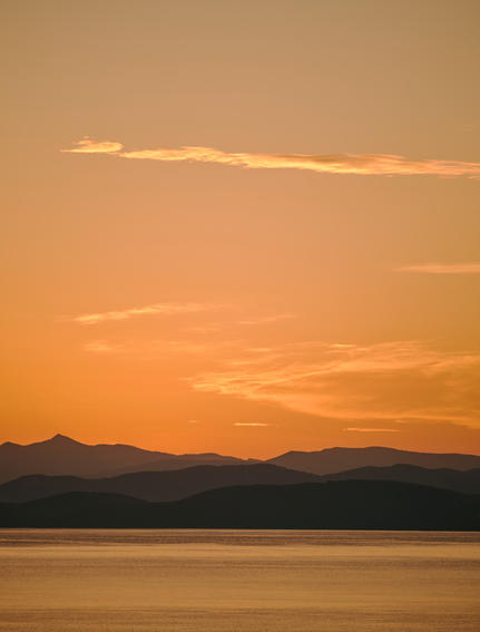 Sunset over calm waters with mountains silhouetted against an amber sky at Amanruya.