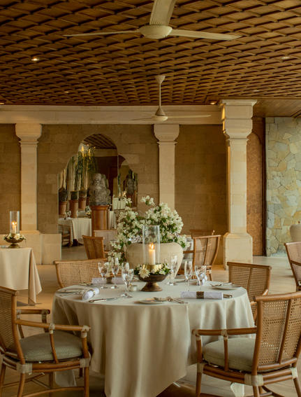 Terrace dining area at Amankila resort with round table, wooden columns, and flowering centrepiece.