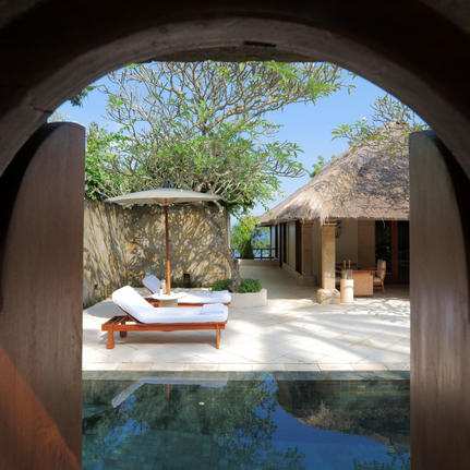 Pool Suite at Amankila resort in Indonesia, framed through curved stone archway with sunbeds and courtyard.