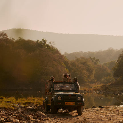 Jeep parked on a riverbank at Aman-i-Khas with forested hills beyond in morning mist.