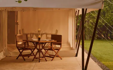 Dining pavilion at Aman-i-Khas with wooden table and chairs opening to manicured lawns.