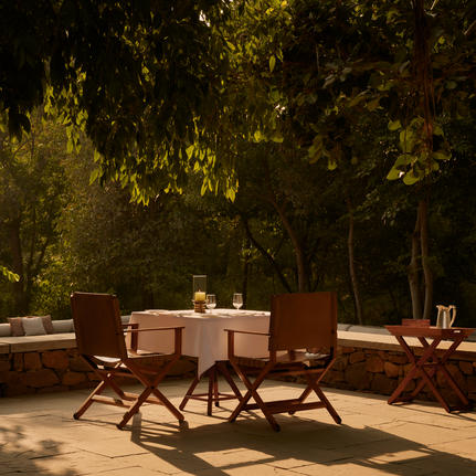 Outdoor dining area at Aman-i-Khas with a table and chairs beneath dappled tree shade.