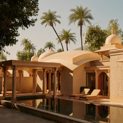Pool pavilion at Amanbagh with terracotta dome and wooden columns, framed by palm trees.