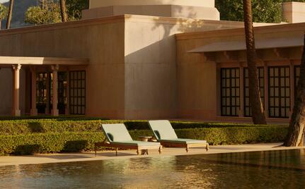Two loungers on a manicured lawn beside a still pool at Amanbagh, India, with earth-toned pavilions beyond.