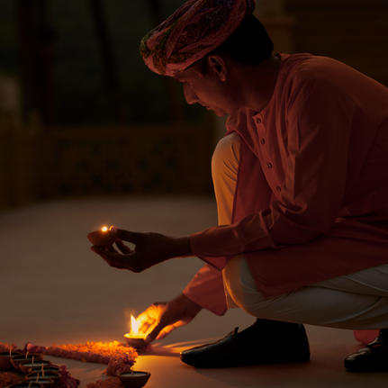 Artisan creating a traditional rangoli pattern by candlelight at Amanbagh.