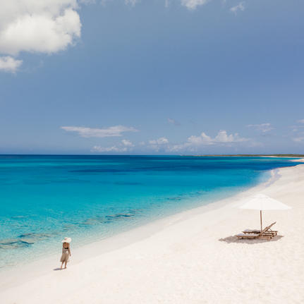 Plage de sable blanc et eaux turquoise à Amanyara resort, avec un voilier traditionnel amarré près du rivage.