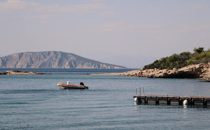 Amanzoe resort beach club overlooking calm Aegean waters and distant coastal cliffs.