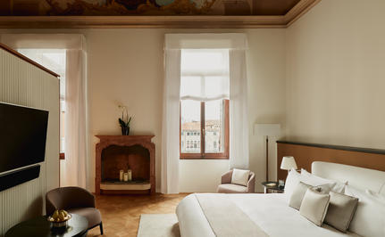 Bedroom at Aman Venice with wooden bed, neutral tones, and tall windows overlooking the city.
