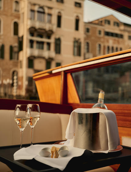 アマン ヴェニスのボートでシャンパンを冷やし、ベネチアの歴史的建造物を背景にアペリティーボを楽しむ。