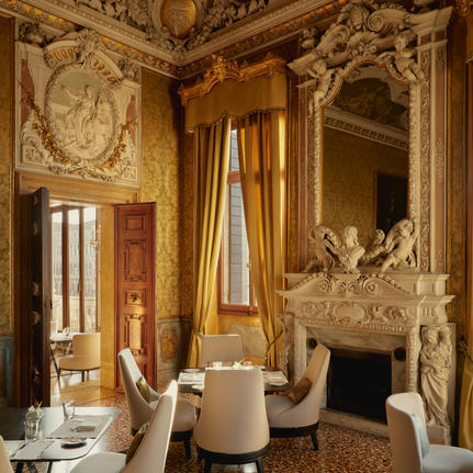 アマン ヴェニスのホテル内にある、金色の装飾と暖炉を備えた優雅なラウンジ。