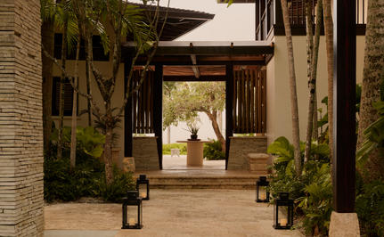 Covered walkway with wooden beams and stone walls at Amanera resort, potted plants flanking the passage.