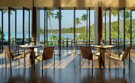 Amanwella restaurant with floor-to-ceiling windows overlooking the Indian Ocean and wooden dining tables.