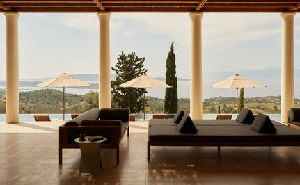 Villa interior at Amanzoe with expansive windows framing Aegean Sea views and cypress trees.