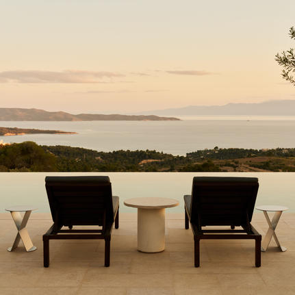 Two black chairs facing calm waters at Amanzoe at dusk, with distant coastline visible.