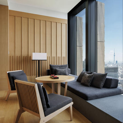 Tokyo Suite lounge at Aman Tokyo with wooden desk, chair, and floor-to-ceiling windows overlooking the city skyline.