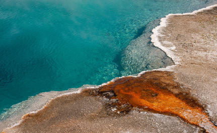Aerial view of a geothermal hot spring with vivid orange and turquoise waters at Amangani, overlooking Yellowstone National Park.