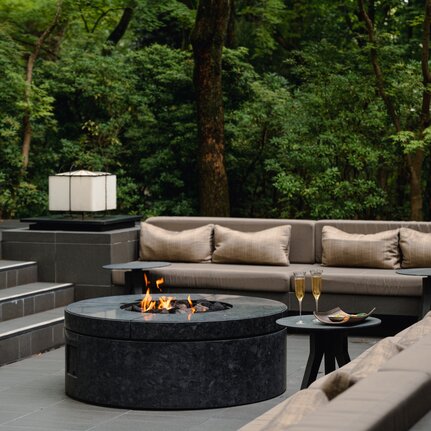 Outdoor aperitif setting at Aman Kyoto with fire pit, seating and verdant garden backdrop.