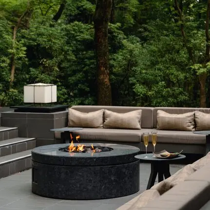 Aperitif seating area with circular fire pit at Aman Kyoto resort, surrounded by tall trees.