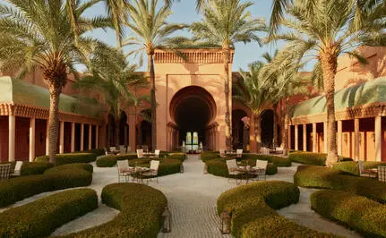 Bar extérieur d'Amanjena, resort au Maroc, avec colonnade, palmiers et bassin central.
