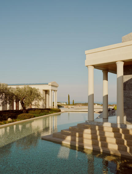 Amanzoe's waterfront canal reflecting classical columns under clear Greek skies in Porto Heli.