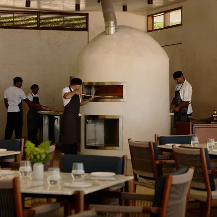 Amanera resort's beach club interior with guests gathered around a central fireplace, wooden dining furniture, and natural light from windows.