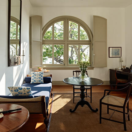 Sunlit suite at Amangalla with arched windows, wooden furniture, and seated area overlooking gardens.