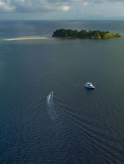 Aerial view of a speedboat approaching a small forested island in Saleh Bay, Sumbawa, Indonesia, where Amanwana is located.