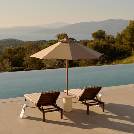 Two sun loungers beneath a parasol beside an infinity pool overlooking forested hills at Amanzoe.