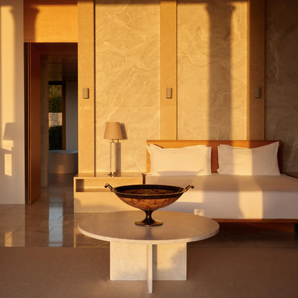 Principal bedroom at Amanzoe with warm limestone walls and minimalist furnishings bathed in golden light.