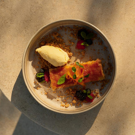 Overhead view of a dessert bowl at Amanzoe beach club restaurant, featuring caramelised cake, berries, and vanilla ice cream.