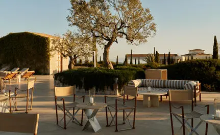 Outdoor dining terrace at Amanzoe with stone tables and chairs at sunset, overlooking Greek countryside.