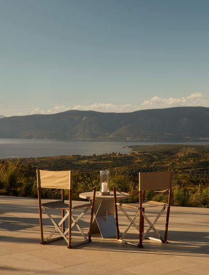 Two chairs on a terrace at Nama restaurant overlooking the Aegean Sea and mountains at Amanzoe, Greece.