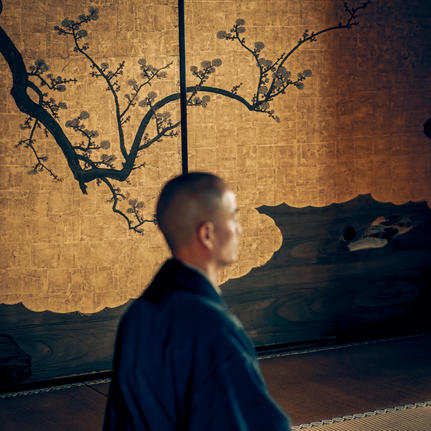 Man in profile before gold-toned artwork depicting bare branches at Aman Kyoto.