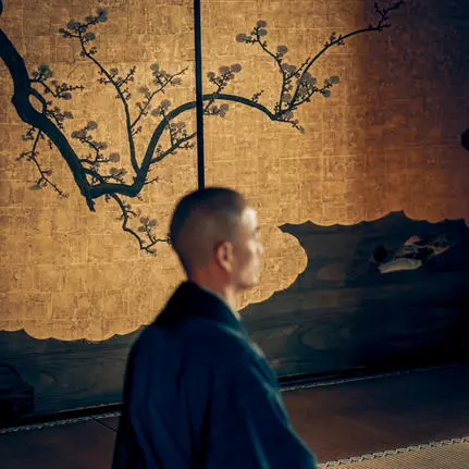 Man in meditation pose beside zen artwork at Aman Kyoto resort.
