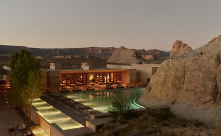 Amangiri resort pool at dusk, with warm-lit architecture nestled between desert rock formations.