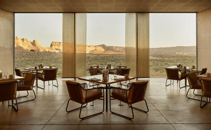 Amangiri restaurant with floor-to-ceiling windows overlooking desert landscape, round dining tables and burgundy chairs.