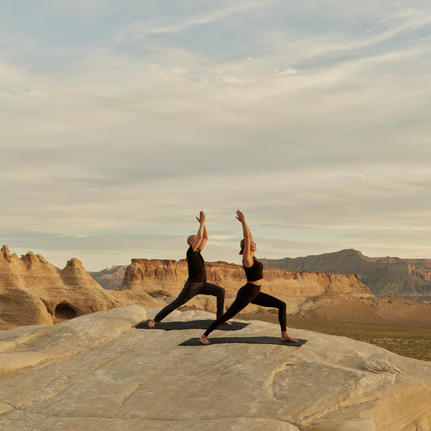 Two people practising yoga on a rock formation at Amangiri, with desert landscape and mountains in the background.