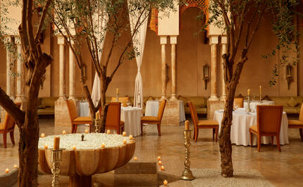 Dining venue at Amanjena resort with tables dressed in white linens beneath arched stone archways and warm lighting.