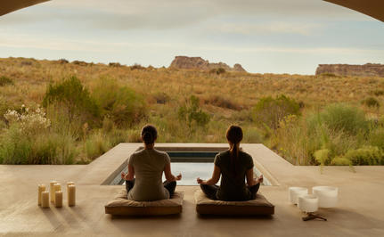 Two guests meditate in an open pavilion at Amangiri, overlooking desert landscape and rock formations.
